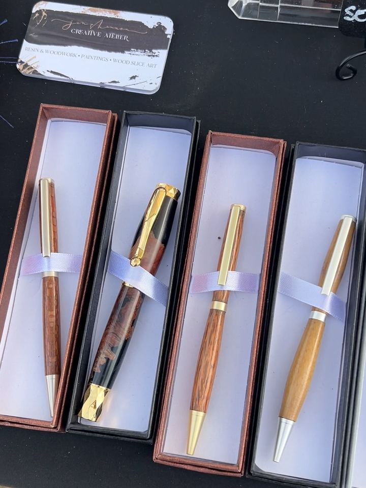 Four finished pens in gift boxes on a craft fair table next to a Jen Shannon Creative Atelier business card