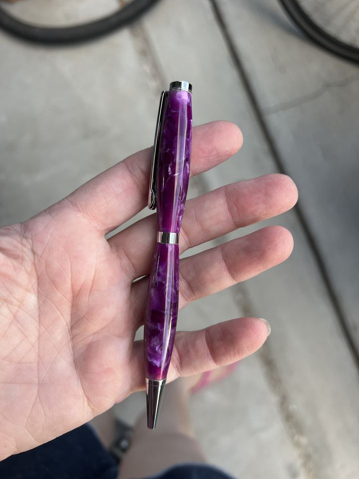 Purple resin pen with silver hardware resting on an open palm